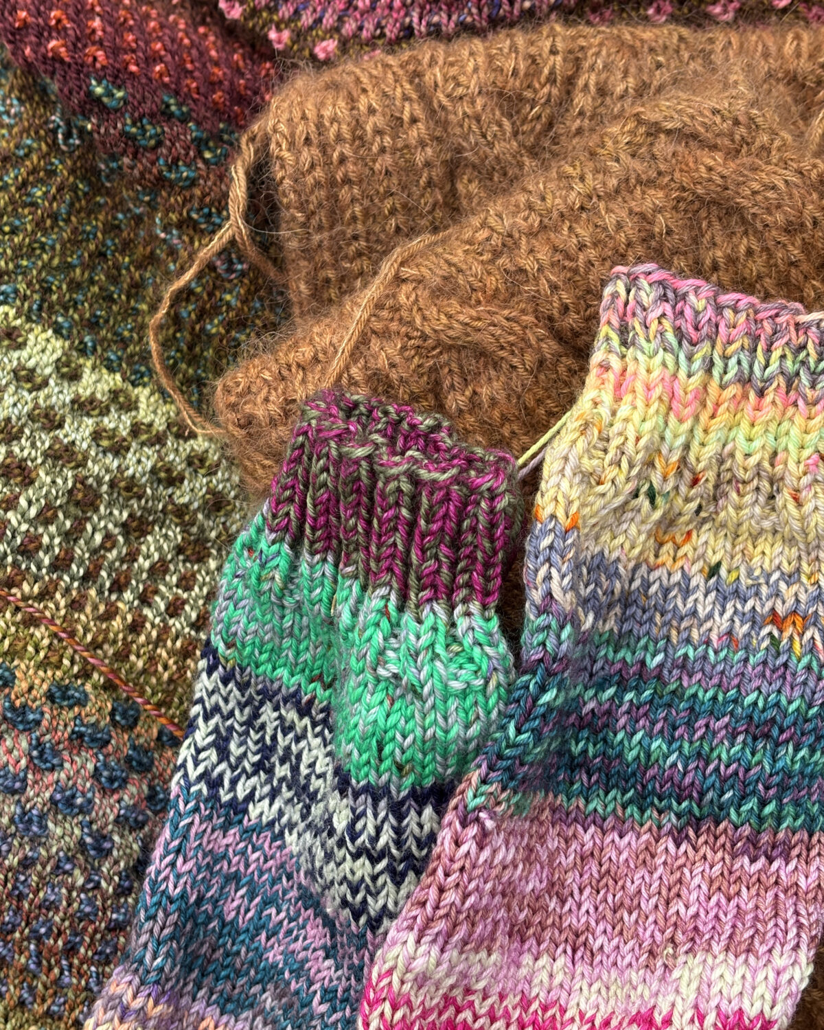 Close-up of multicolored knitted yarns and fabric textures in pink, green, blue and brown tones.